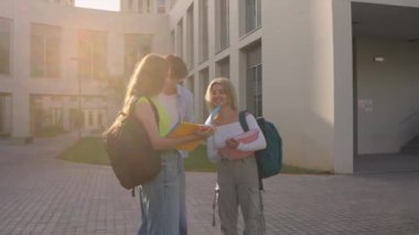 Üç üniversite öğrencisi bir üniversite binasının önünde notları gözden geçiriyorlar ve tartışıyorlar.