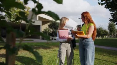 İki kız öğrenci notlarını karşılaştırıyor ve dışarıda, okul kampüsünde sohbet ediyorlar.