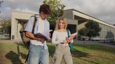 İki üniversite öğrencisi kampüste yürüyor, notları tartışıyor ve parlak, güneşli bir ortamda fikirleri paylaşıyorlar.