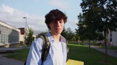 Sırt çantası ve kitaplarla kampüste yürüyen gülümseyen bir üniversite öğrencisi. Güneşli bir günün tadını çıkarıyor ve derslerinden emin.