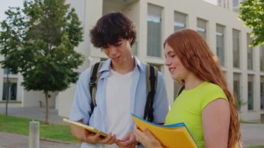 İki üniversite öğrencisi güneşli bir günde bir tablet ve kitaplar kullanarak bir proje üzerinde birlikte çalışıyorlar.