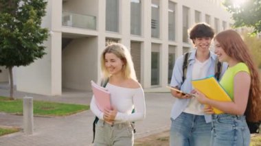 Üniversite öğrencileri kampüste tablet kullanırken tartışıyorlar, güneşli bir günün tadını çıkarıyorlar.