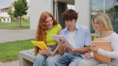 Üç üniversite öğrencisi sonbahar boyunca güneşli bir kampüs bankında birlikte otururken çalışmalarda işbirliği yapıyorlar.