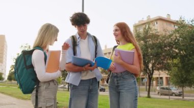 Güneşli gökyüzünün altında canlı bir üniversite kampüsünde dururken üç genç yetişkinin notları inceleniyor ve gülücükleri paylaşılıyor.