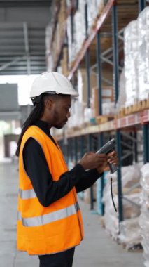 Portakal rengi güvenlik yeleği giyen bir depo işçisi ağır çekimde el bilgisayarı kullanarak envanter taraması yapıyor.