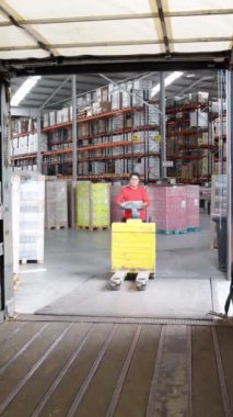 Bir depo çalışanının lojistik merkez yükleme alanında mal taşırken sarı bir palet krikosunu dikkatlice kullanmasının yavaş çekim görüntüleri.