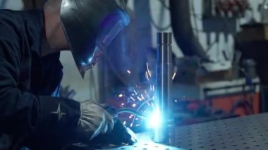 Bir atölyede güvenlik malzemesi takan metal işçisi, bir meşale ve hassas ekipman ile kıvılcımlar yaratıyor.