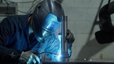 Güvenlik ekipmanı takan kaynakçı kaynak makinesi kullanarak metal bileşenleri birleştiriyor ve parlak kıvılcımlar üretiyor.