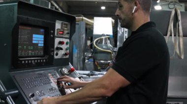 Siyah gömlekli bir fabrika işçisi, bir cnc makinesi çalıştırıyor, dikkatle komutları giriyor ve süreci izliyor