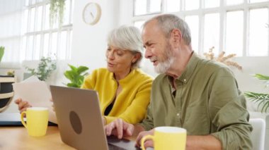 Olgun bir çift masada oturur, parlak ve rahat bir ev ortamında dizüstü bilgisayar kullanırken evrak işlerini tartışırlar.