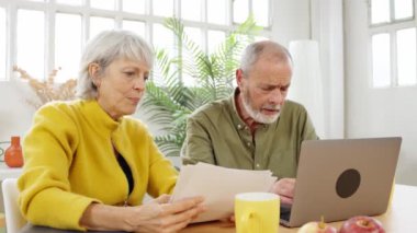 Olgun bir çift mutfak masasında oturmuş, önemli belgeleri tartışıyor ve birlikte dizüstü bilgisayar üzerinde çalışıyorlar.