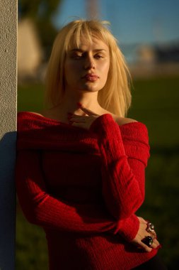 Ukraynalı manken, altın saat fotoğraf çekiminde şık kırmızı bir kazakla poz veriyor, zarafet ve kendine güven yayıyor.