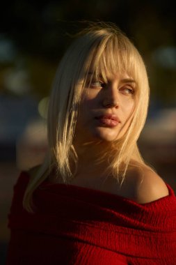 Sarışın Ukraynalı model, omuzları açık kırmızı bir elbise giyiyor, altın saat fotoğraf çekiminde poz veriyor, modaya uygun ve anımsatıcı bir görüntü yaratıyor.