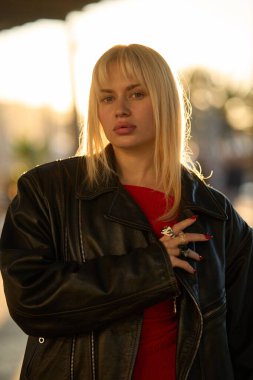 Moda fotoşopu sırasında kırmızı elbise ve siyah deri ceket giyen sarışın Ukraynalı bir manken.