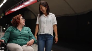 Tekerlekli sandalyedeki neşeli kadın metro istasyonunda arkadaşıyla sohbet ediyor, gülüşünü ve gülüşünü paylaşıyor.