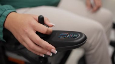 Elektrikli sandalyesini kontrol etmek için joystick kullanan bir kadının yakın plan çekimi, cihazı yönetmek için odak ve beceri gösteriyor
