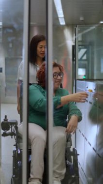 Hemşire, tekerlekli sandalyedeki bir kadına turnikede yol göstererek ulaşılabilirliği ve desteği ön plana çıkarıyor.