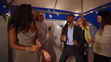 Canlı bir çatı partisinde kutlama yapan arkadaşlar, telli ışıkların altında enerjik bir şekilde dans edenler. Çeşitli gruplar müzik ve içeceklerin tadını çıkarıyor, birlikte geçirdiğimiz neşeli anları yakalıyorlar.