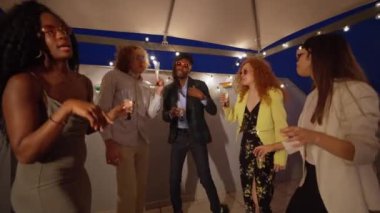 Bir grup farklı arkadaş coşkulu bir çatı partisinde kutlama yaparken içki ve kahkahaların tadını çıkarıyorlar.