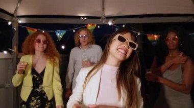 Dans eden kadın, arkadaşlarıyla çevrili canlı bir çatı partisinden hoşlanıyor. Şehir ışıkları altında kutlama, içki ve müzikle kutlanıyor.