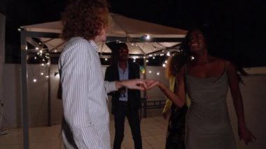 Çeşitli arkadaşlar canlı bir çatı partisinin tadını çıkarıyorlar. Gece gökyüzünün altında dans edip kutluyorlar.