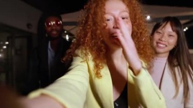 Kızıl saçlı kadın arkadaşlarıyla eğlenceli bir selfie çekerken parlak ışıklar altında canlı bir partide kutlama yapıyor.