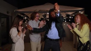 Zarif giyimli bir grup arkadaş ip ışıklarının altında neşeyle dans eder, bir yaz akşamında birlikte kutlama yaparlar.