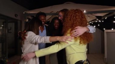 Bir grup arkadaş şehrin ışıkları altında canlı bir çatı partisinde kucaklaşıp kutluyorlar.