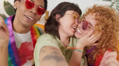 Üç neşeli Igbtq arkadaşı gökkuşağı bayrakları takıyor komik bir selfie çekiyorlar ve kamerayı yavaş çekimde öpüyorlar.
