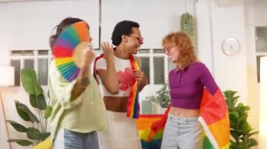 Gururu kutlayan üç arkadaş gökkuşağı bayrakları ve hayranlarıyla neşeli bir şekilde dans ediyorlar.