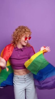 Lgbtq aktivisti gökkuşağı bayrağı sallıyor, kalp şeklinde güneş gözlüğü takıyor, parlak mor bir arka plana karşı.
