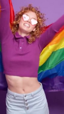 Gökkuşağı bayrağı sallayan neşeli lgbtq eylemcisi, mor arka planda gurur ve çeşitliliği yavaş çekimde kutluyor