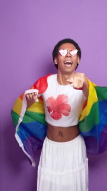 Gökkuşağı bayrağıyla mor zemin üzerinde dans eden neşeli, ikili olmayan aktivist, lgbtq gururunu yavaş çekimde kutluyor.