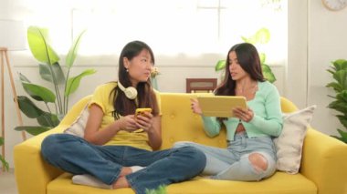 Dijital teknolojiyle bağlantı kuran genç kadınlar, sarı koltukta otururken, aydınlık ve modern oturma odasında içeriklerine göz atıyorlar.