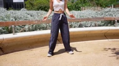 Dinamik serbest stil hip hop hareketleri yapan kadın dansçı, şehir planına karşı park alanında duruyor.
