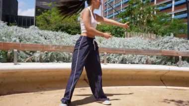 Şehir parkında tutkuyla dans eden kadın dansçı, dinamik hareket yoluyla özgürlük ve neşe ifade eden, şehir manzarası arasında pozitif enerji yayan