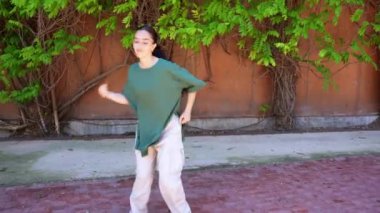 Genç bayan dansçı, sarmaşık kaplı şehir duvarına karşı serbest hip hop hareketi sergiliyor. Güneşli bir günde canlı enerji ve sanatsal tutku ifade ediyor.