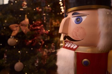 Arka planda Noel ağacı olan klasik bir fındıkkıran figürünün yakın çekimi, bayram atmosferi yaratıyor.