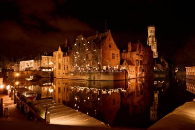 Illuminated buildings and christmas lights reflecting on the dijver canal in bruges, belgium, at night clipart