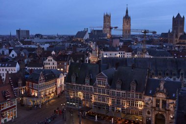 The cityscape of ghent, belgium glows under twilight sky, featuring the prominent saint bavo cathedral and saint nicholas church clipart