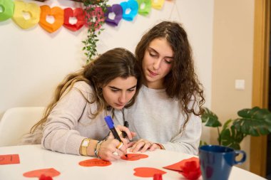 İki kadın kalp şeklinde kartlara romantik mesajlar yazıyorlar. Sıcak bir ev ortamında sevgililer gününe hazırlanıyorlar.