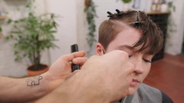 Profesyonel kuaför dikkatli bir şekilde müşterilerin saçlarını kesiyor. Modern salon ortamında yavaş çekim tekniğiyle çağdaş saç stili yaratıyor.