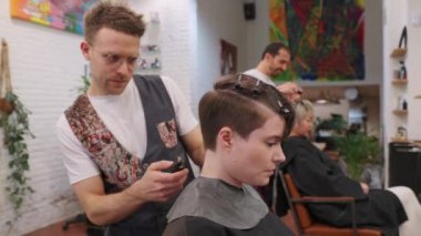 Profesyonel kuaför kadın müşterilerinin saçlarını makas ve hassasiyetle kesiyor, modern, renkli salon ortamında yavaş çekim detaylarıyla şık kısa saç stili yaratıyor.