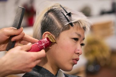 Kuaför kuaför kuaförde kısa sarı saçlı genç bir kadının saçını kesmek için saç makası kullanıyor.