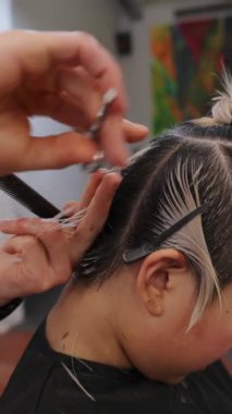 Profesyonel kuaför dikkatli bir şekilde ıslak sarı saçlarını hassas bir makasla kesiyor, yavaş çekim salonunda çağdaş saç stili yapıyor.