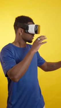 VR kulaklık takan genç adam sanal dünyayı keşfediyor, canlı sarı arkaplan karşısında dijital çevreyle etkileşime geçiyor