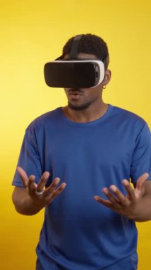 VR kulaklık takan genç adam, sarı arka planda el hareketleriyle sanal çevreyle etkileşime giriyor.