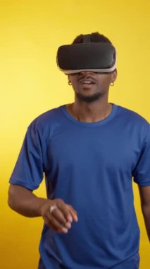 Meraklı bir adam sanal gerçeklik kulaklığıyla etkileşime geçiyor, canlı sarı bir arka plana karşı etkileyici bir teknoloji deneyimliyor.