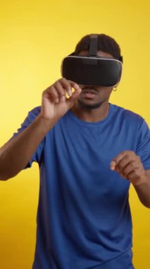 VR kulaklık kullanan, sanal gerçekliği deneyimleyen ve sarı arka planda dijital dünyayla etkileşimde bulunan hevesli genç bir adam.