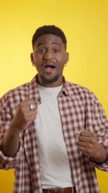 Mutlu genç adam dans ediyor ve neşeli sarı bir arka planda eğleniyor, neşe ve kaygısız tavır sergiliyor.